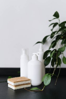 Fotokopi alanı olan beyaz plastik deterjan şişeleri ve siyah tezgahta çevre dostu bulaşık süngerleri, mutfak temizliği konsepti.