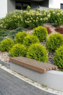 Boş beton tezgahın dikey çekimi, yeni tahta levhalarla dinlenme alanında çimen ve çiçeklerle manzara tasarımına karşı oturmak için. Şehir parkında sandalyeli konut binasının yanındaki bahçe.