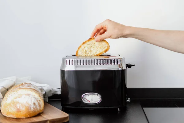 stock image electric toaster on black countertop at home kitchen with white wall and female hand put slice bread for making crispy toast for breakfast, cooking concept