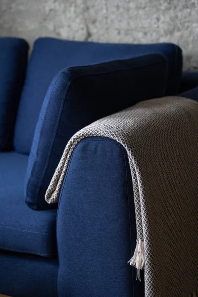 closeup of comfortable sofa with pillows and warm blanket neatly folded on armrest at living room in apartment with loft interior, furniture in blue upholstery