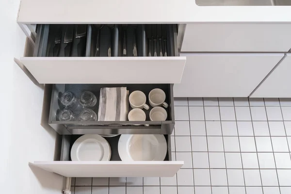 keeping silverware in separated container at shelf in cabinet, open drawers with clean forks, spoons, plates, cups and glasses, organized space at home interior, above view