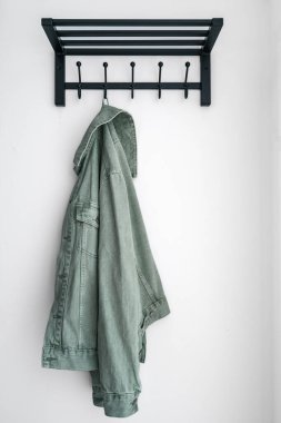 Yeşil kot ceketin dikey görüntüsü koridorda asılı duruyor. Başlık için boş rafı olan siyah metal bir elbise askısı ve apartman odasındaki ya da koridordaki beyaz duvara günlük kıyafet montajı.