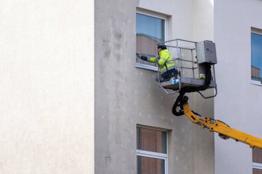 Vinç platformunun üzerinde duran dış bina boyama işi yapan profesyonel bir işçi. Ev tadilatı ve yenileme konseptleri. Adamın biri evinin ön cephesini boyuyor.