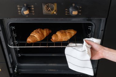 Modern mutfaktaki metal fırın rafında sıcak taze kruvasan tutan bir kadın eli. Ev yapımı kavram.