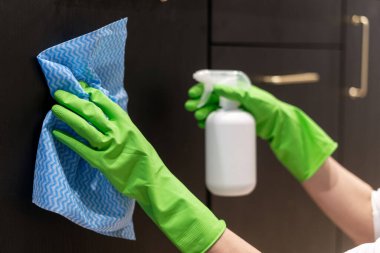 Yeşil lastik eldivenli kadın ellerinin kesilmiş görüntüsü deterjan spreyi şişesi ve ev mutfağındaki dolapların ahşap kapılarını temizlemek için bez bez parçası, ev işi konsepti.