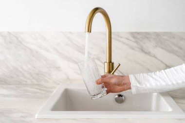 Kırpılmış kadın el kamerası bardağı ve filtrelenmiş suyu mutfak arka planında karıştırıcı musluktan doldurmak, sağlıklı yaşam tarzı konsepti