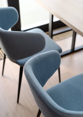 Modern yemek odasının iç kısımlarında detay, tekstil döşemeli yumuşak sandalyeler ve ahşap yüzeyi olan masa arkasında rahatlık.