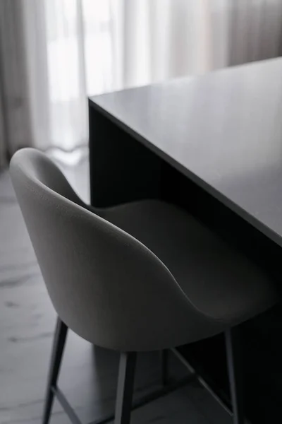 closeup of soft chair with back and grey textile upholstery near table at room with contemporary interior, home office workplace concept