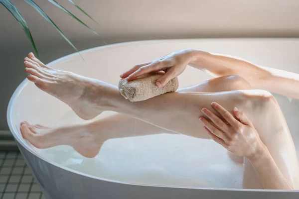 Cropped view of woman washing her legs in bath, using soft sponge. Skin, body and self care routine. Beauty concepts and home spa procedure. Female pampering feet after shaved