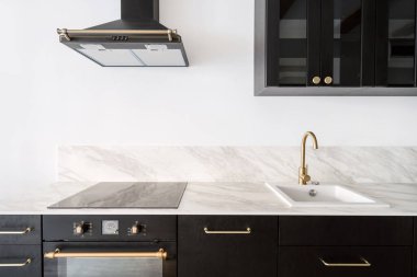 luxury interior at home kitchen, new wooden cupboard, electric oven, induction hob on marble countertop, white sink, water faucet and cooker hood