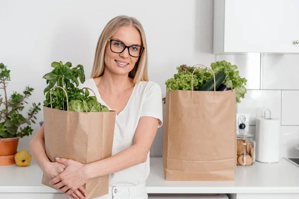 smiling female hold eco friendly shopping bag with fresh salad leaves, lettuce and green herbs at home kitchen, grocery purchase and healthy eating concept