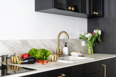 home kitchen interior, induction stove, modern sink, golden faucet, vase with flowers and different vegetables on countertop, cooking concept 
