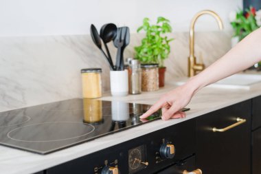cropped shot of female hand press sensor button and using electrical hob for cooking dinner at home kitchen with stylish interior, modern household appliances concept