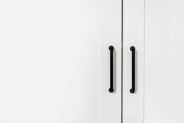 closed white wardrobe with wooden doors and black metal handles in dressing room, modern furniture at home, storage concept