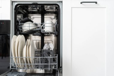 front view on built in dish washing machine with dirty dishware and silverware inside in kitchen with white cabinet furniture and modern interior, integrated appliance