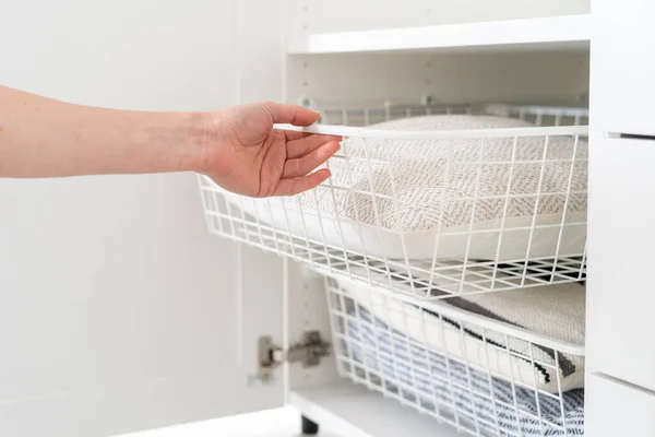 cropped shot of female hand put mesh drawer with bedding linen in wooden closet with open door, Scandinavian storage concept, organized space in dressing room