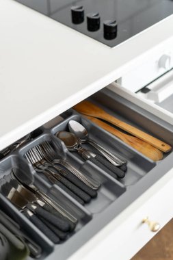 closeup of opened wood drawer of cabinet at modern kitchen with plastic section for keeping clean silverware, spoons, forks, knife and utensils