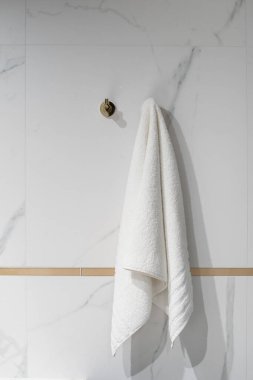 closeup of golden hook and bath towel hanging on wall with marble tile in luxury bathroom, minimalism concept, vertical shot