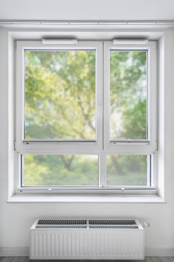 Yeni çift camlı pvc pencere yenilendikten sonra oturma odasında modern katlanmış kör jaluzi ile, bulanık yeşil ağaçlar arka plan görünümlü