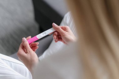 Kadın ellerindeki hamilelik testine yüksek açılı bakış açısı, kontrol et ve sonuç bekle, oturma odasında kanepede otur, geleceği planla.