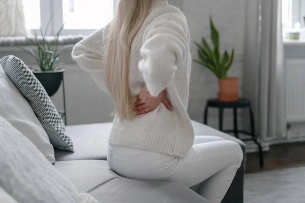 女性は不快感と手で腰椎に触れると背中の問題腎臓痛の女の子はリビングルームのソファに座って 切り取られたショット — ストック写真