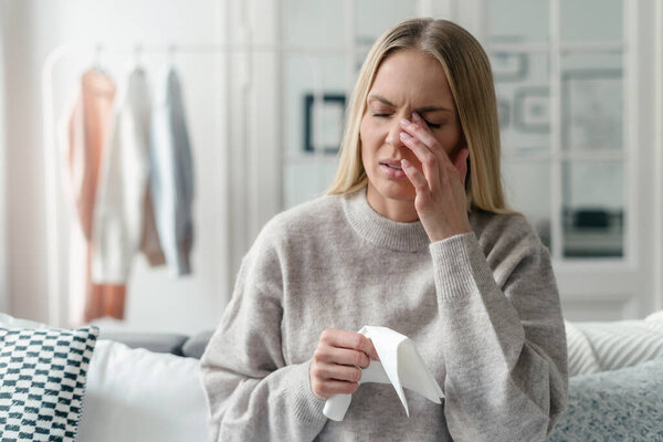 illness woman with fever feeling virus symptom, headache and eyestrain, holding tissue in hand at home apartment