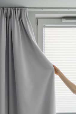 Kırpılmış kadın görüntüsü gri kumaş perde ve pencereyi kapatır. Yatak odasındaki güneş ışığından korunmak için modern iç dekorasyon, ev dekorasyonu.