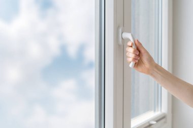 Kadın el tutuşunun kırpılmış görüntüsü ve eve beyaz çerçeveli çift camlı PVC pencereyi kapat, dışarıdaki gürültüden odayı koru 