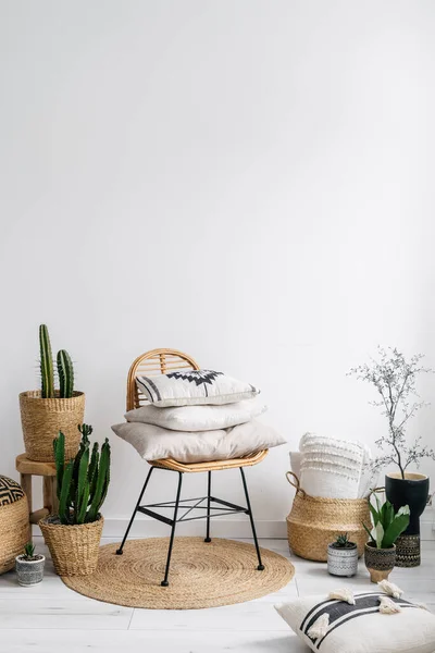 stock image detail in living room with boho interior, stack of cushions in textile covers on rattan chair, wicker basket, pots with houseplants and rug on floor