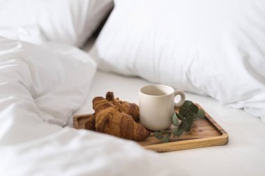 Ahşap tepside bardakta içki ve taze kruvasanlarla süslenmiş okaliptüs dalını beyaz pamuk çarşafa, yastıklara, sabah konseptine yakın tut.