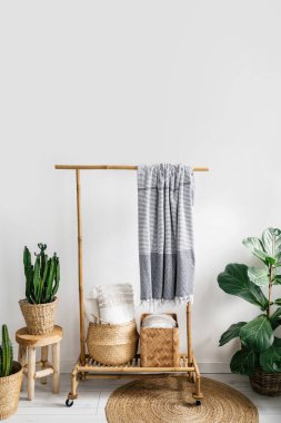 İçi boho kaplı odada detay ahşap elbise askılığında ekose kumaş hasır sepetin içindeki yastıklar saksı bitkileri ve yerde yuvarlak halı, depolama konsepti.