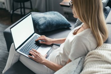 Genç bir bayan internet sitesine girmek için dizüstü bilgisayar kullanıyor, rahat bir koltukta oturuyor ve klavyede, omuz üstü kamera görüntüsü üzerinden daktilo çekiyor. 