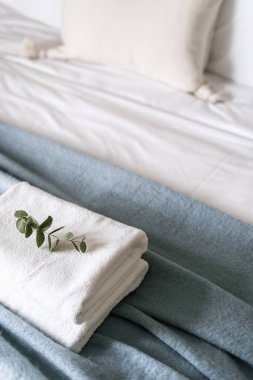 Yatak örtüsü ve battaniyeyle güzelce katlanmış, okaliptüs dalıyla süslenmiş, yatak odasının iç kısmında detaylar, yüksek açılı görüş.