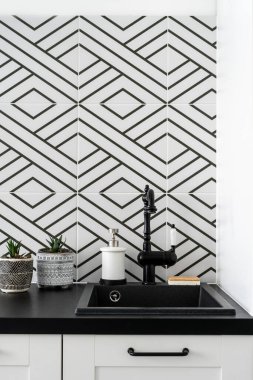 Mutfak içinin ayrıntıları, eski tasarımı olan musluk, lavabonun yanında sabun ve eko sünger temizleyici, tezgahta seramik kaplarda bitkiler, duvarda desenli fayanslar.