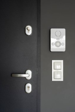 Kilit ve metal saplı kapalı kapı manzarası, ışık anahtarı ve dairede duvarda kontrol düğmesi olan modern kapı telefonu, akıllı dahili iletişim sistemi
