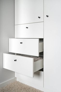 Açık çekmeceleri ve siyah sapları olan beyaz ahşap gardırop, temiz havlular depolama, içinde yatak örtüleri ve giysiler, apartman dairesindeki iç aydınlığı olan modern mobilyalar