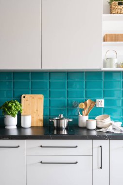 Mutfakta içi rahat, metal saplı beyaz dolap elektrikli fırında tencere, seramik saklama kavanozları ve siyah tezgahta temiz kaseler.