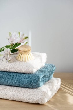 Katlanmış, temiz yumuşak havlular, küçük bambu fırçası ve ahşap bej masadaki çiçek. Gün ışığı ve gölgeler banyoda. Hijyen kavramı
