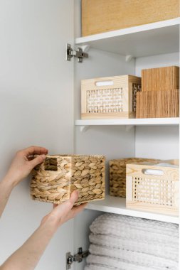 Kırpılmış kadın eli hasır sepetini tutar ve temiz çarşaflar ve temiz havlular ile birlikte rafa koyar. Organize uzay kavramı.
