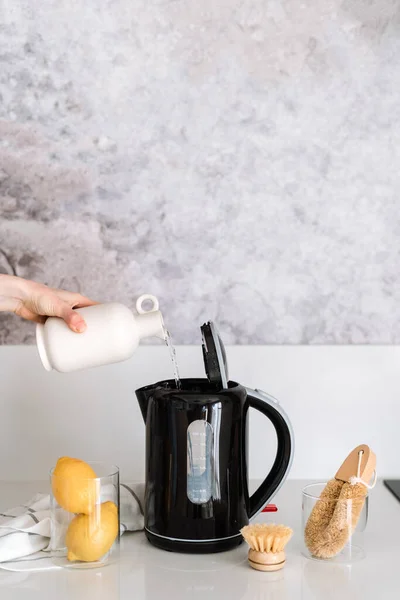 Descaling calcified black electric kettle with water, lemons and brushes on white top. Grey marble background. Housework problem and solution.