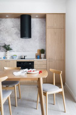 Modern dolap mobilyaları ve ev aletleriyle şık mutfakta ahşap masa ve rahat sandalyeler yemek.