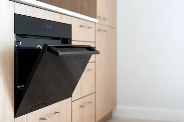 stock image Selective focus on new oven with open door against white copy space background in kitchen. Side view of modern design of induction cooker in apartment