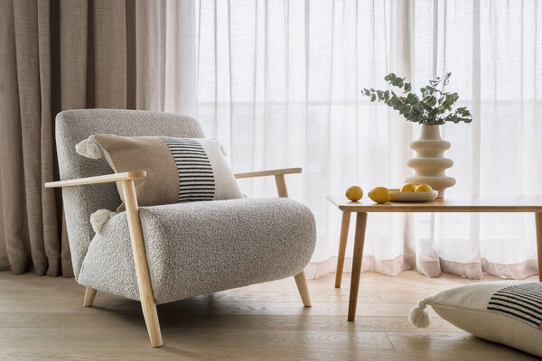 Home decor and furnishing concepts. Elegant armchair with cushions in bohemian style near wooden table with lemons and flowers in white geometric vase. Expensive design objects in apartment interior