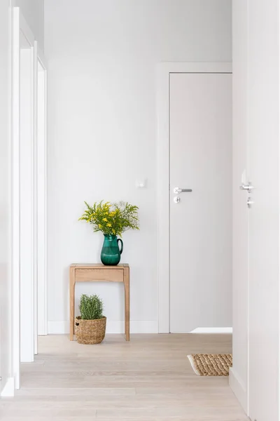 廊下の白い閉じた部屋のドア光のインテリア 木製のベッドサイドテーブルの上に花とガラス花瓶や床に植物とウィッカーバスケット — ストック写真