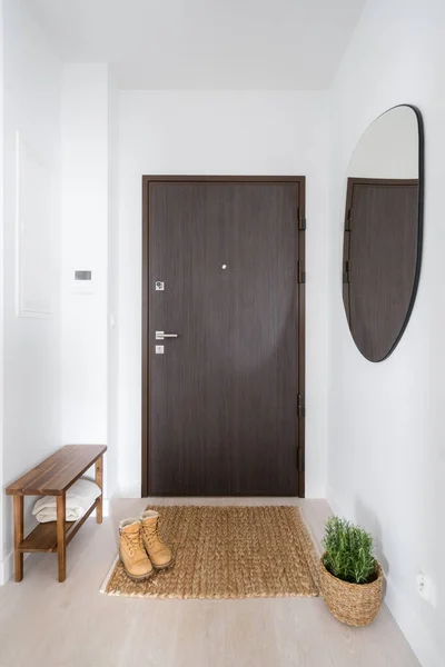 ミニマリズムスタイル 入り口のドア 床のカーペットの上の靴 快適な木製のベンチ ウィッカーバスケットの植物や白い壁のミラーと居心地の良い玄関 — ストック写真