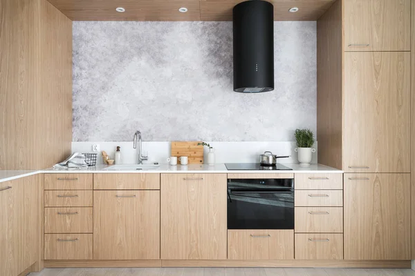 wooden cabinet furniture with white worktop, electric oven, induction stove, hood extractor, sink with water tap and kitchenware at kitchen with modern style
