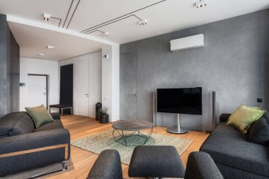 Gri konforlu kanepesi, ergonomik koltuğu, sehpası ve şık bir dairesi olan büyük bir televizyon ekranı olan bir otel odası. Mobilya fikri, modern bina konsepti.