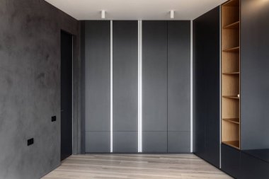 Dairenin içinde modern bir iç mekan, raflı kıyafet dolabı, çatı katı tarzı beton duvar ve ahşap kaplama zemin.