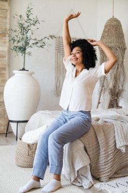 Mutlu Afro-Amerikalı kadın uyandı, rahat yatak odasında ellerini kaldırarak uzandı, enerjiyle yeni bir güne başladı, iyi hissetti ve günaydın. sağlıklı uyku kavramı