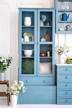 Tek renkli mavi mutfak var. Dekorasyon unsurları olan tahta dolapların dikey çekimi. Ev dekoruna yakın vazolarda taze çiçekler çaydanlıklar ve kavanozlar. İç mekanda eski kaynak biçimi